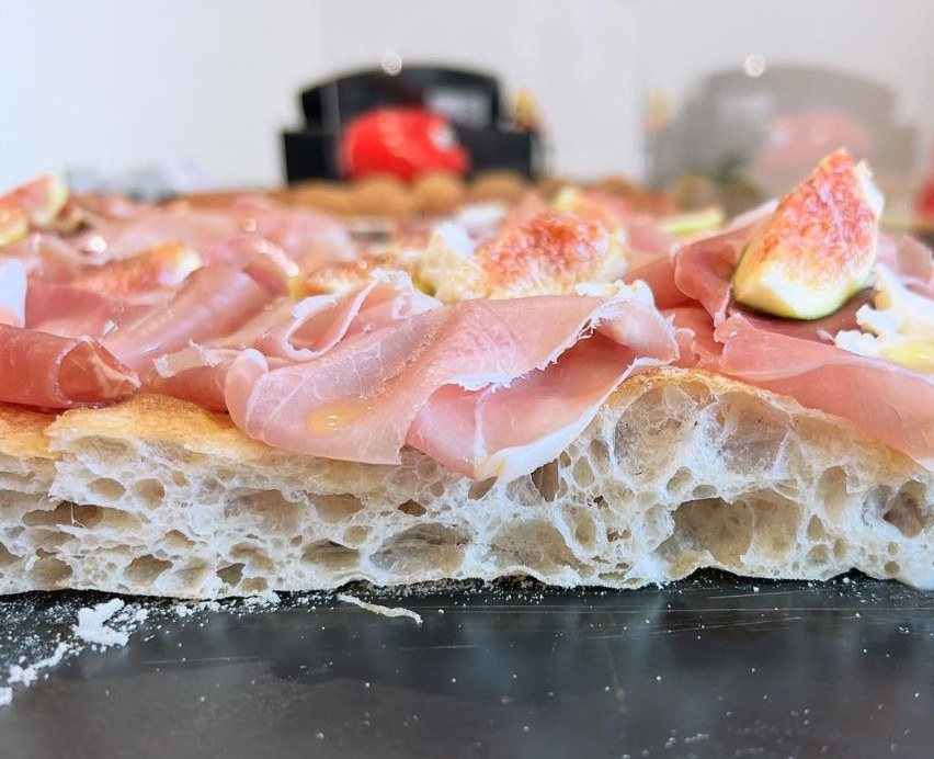 Sezione di un trancio di pizza in teglia con alveolatura evidente, prosciutto crudo e fichi