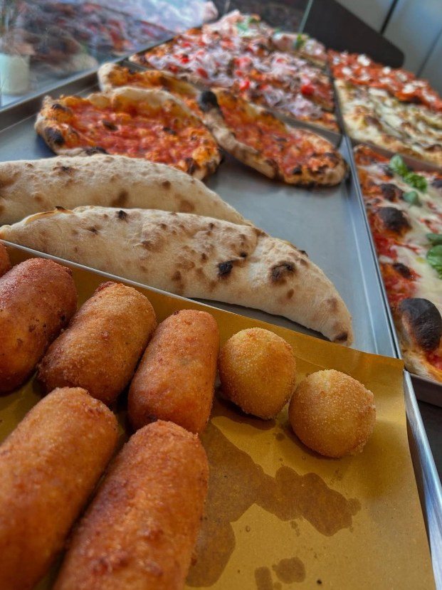 Crocchette e arancini su carta dorata, calzoni e teglie di pizza al pomodoro e basilico nel banco di BIGA Pizza al Taglio